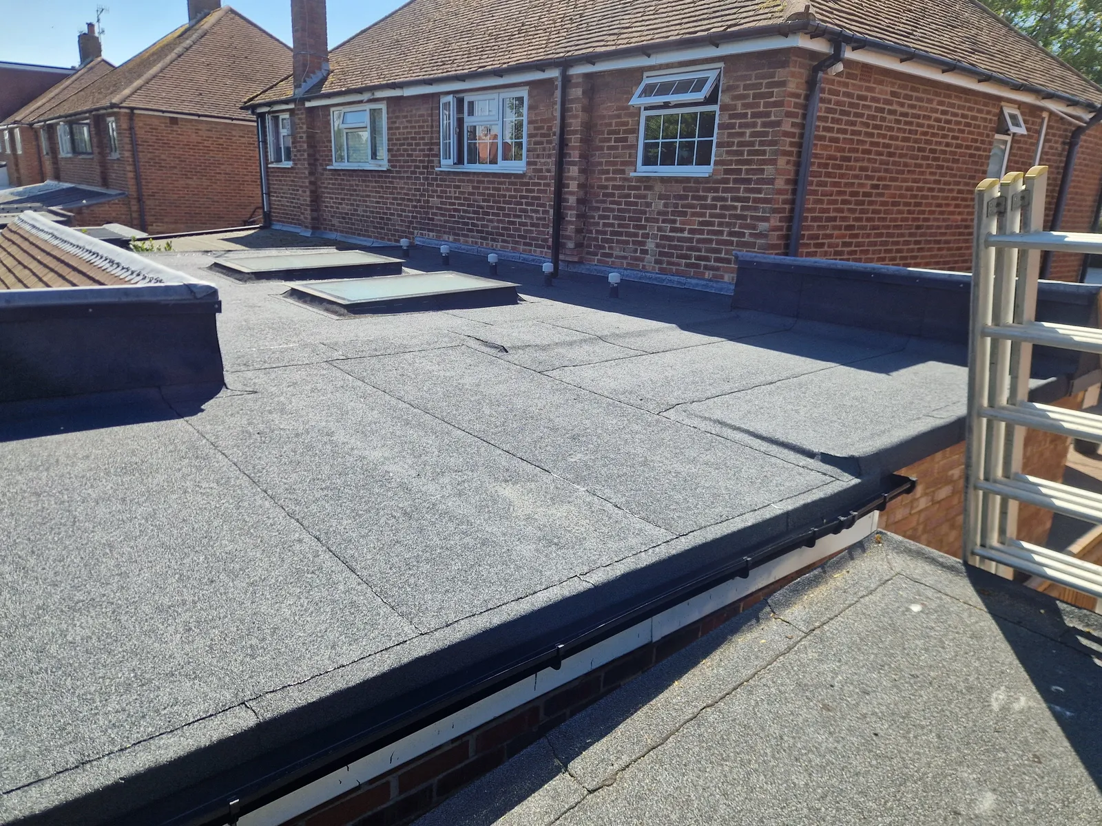 A finished mineral felt flat roof behind a bungalow, with two roof lights and vents