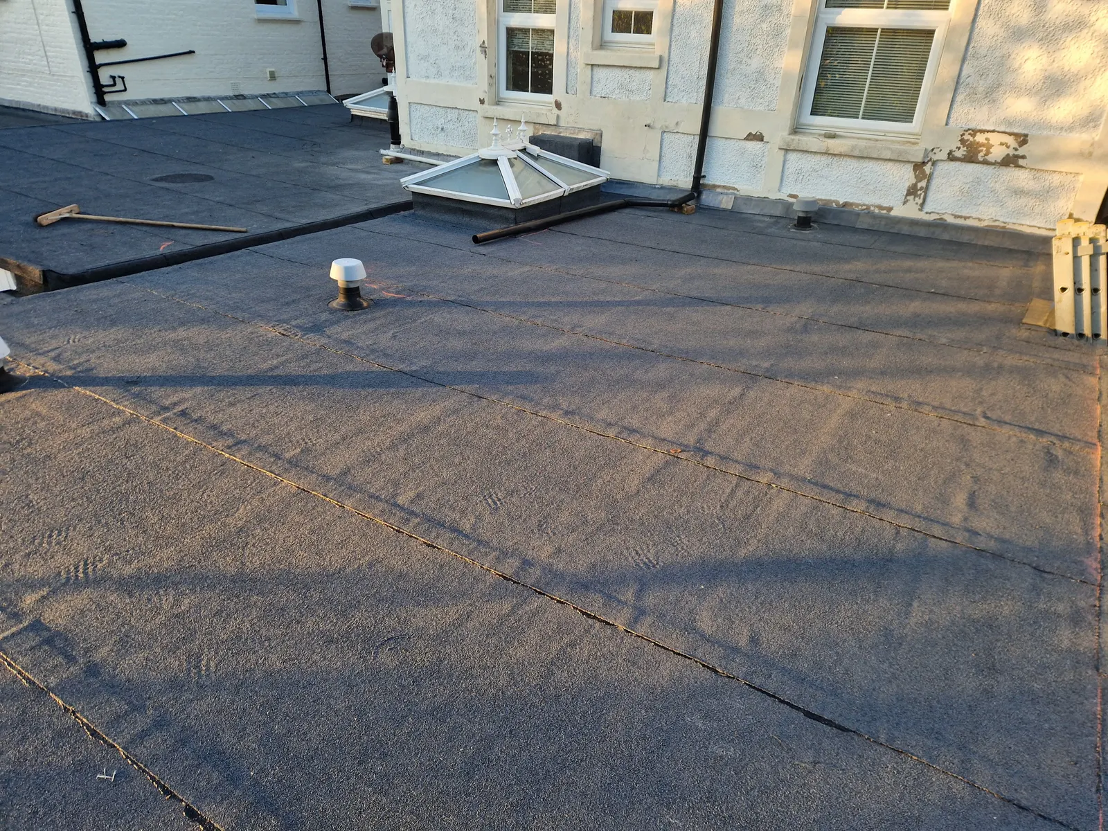 A finished mineral felt covering across a large flat roof with a roof lantern