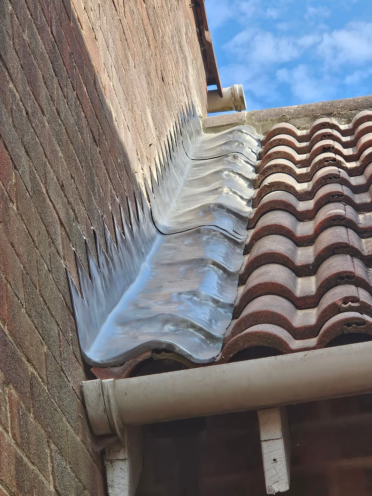 New lead flashing dressed over the roof tiles and up the house wall, where a garage roof meets the house