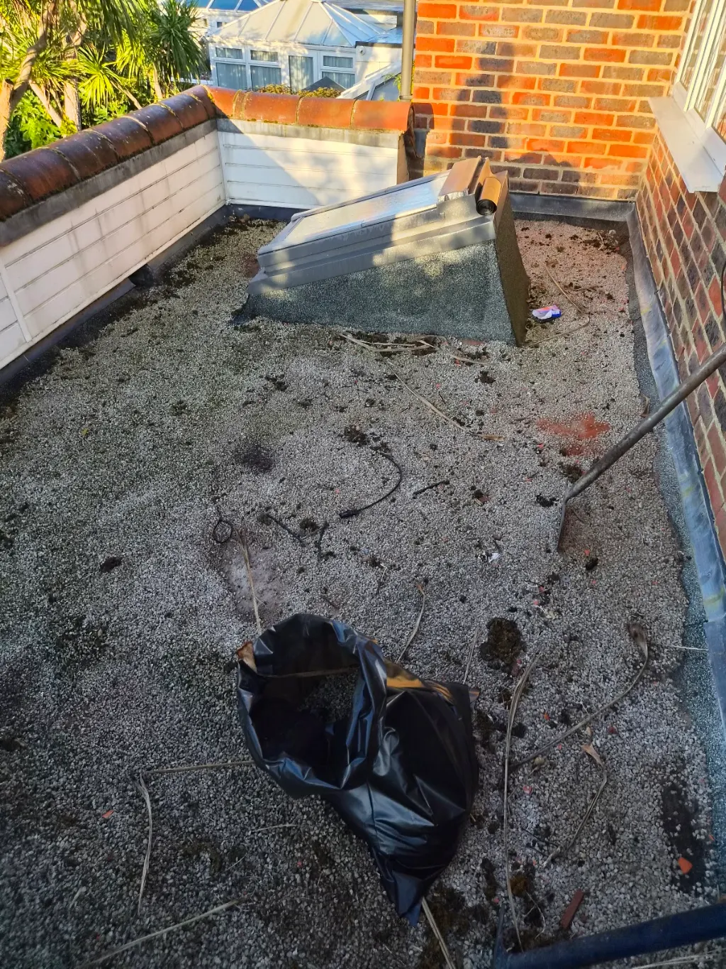 Flat roof covered in loose gravel and debris around a roof light, before its new covering